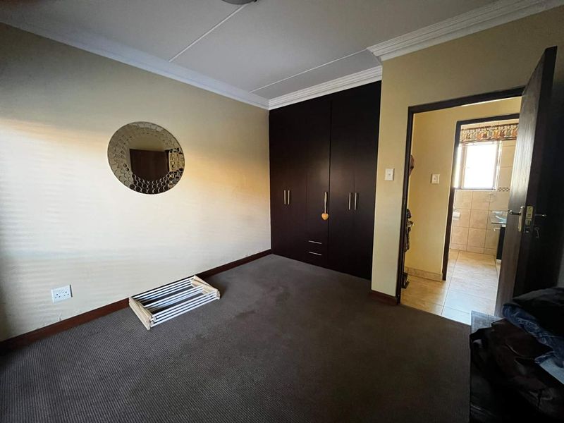 A carpeted bedroom featuring built-in dark wood cupboards and access to an adjoining bathroom.