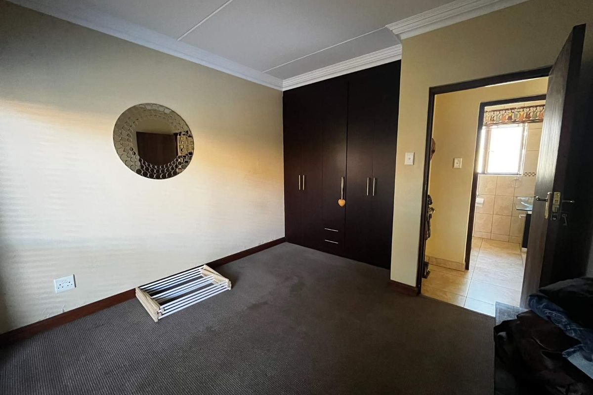 A carpeted bedroom featuring built-in dark wood cupboards and access to an adjoining bathroom.