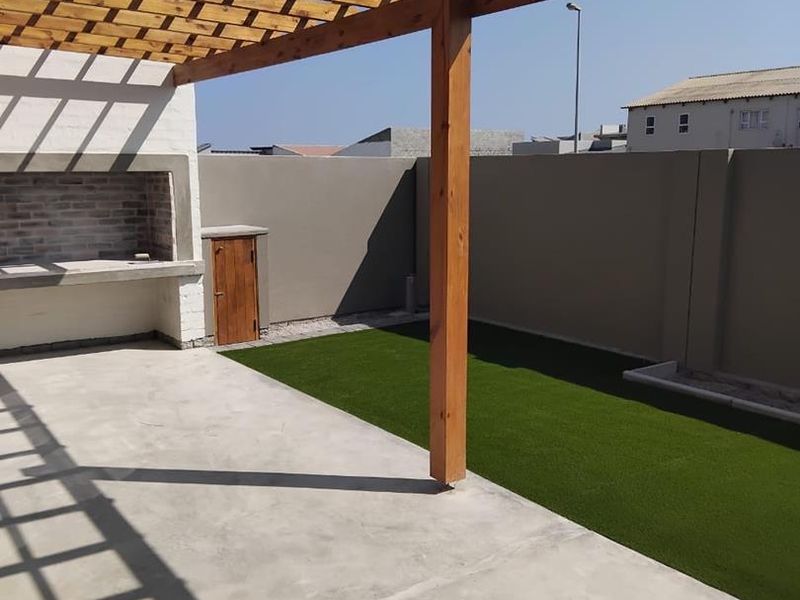 Outdoor patio area featuring a wooden pergola, built-in braai, concrete flooring, and a low-maintenance artificial grass lawn enclosed by perimeter walls.