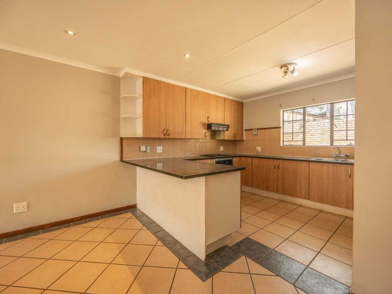 A functional kitchen featuring light wood cabinetry, granite countertops, a built-in hob with extractor, and tiled flooring in an open-plan layout.