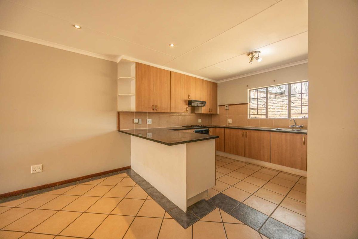 A functional kitchen featuring light wood cabinetry, granite countertops, a built-in hob with extractor, and tiled flooring in an open-plan layout.