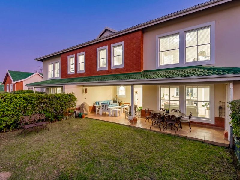A well-maintained rear exterior view of the townhouse featuring a covered patio, tiled flooring, and a landscaped garden area.