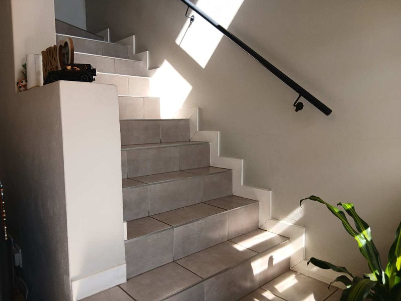 A clean, tiled staircase featuring a modern black metal handrail, providing a functional and well-maintained transition between levels in the townhouse.