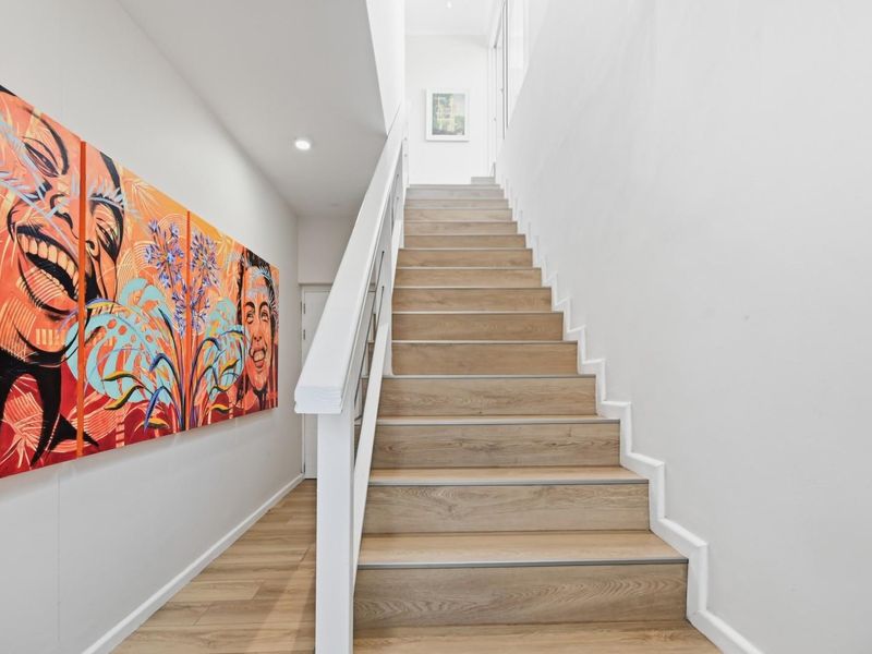 A bright and modern hallway featuring a clean staircase with timber-look treads and a white balustrade, leading to an upper level.