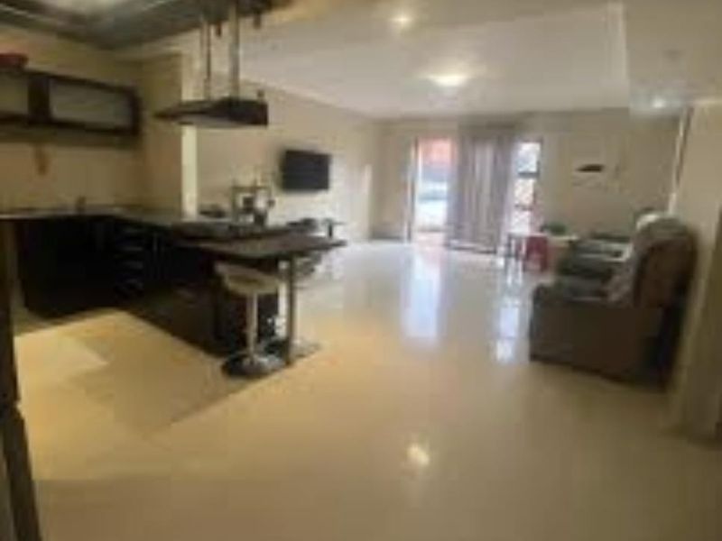 Open-plan living area featuring a kitchen with dark cabinetry, a breakfast island, and tiled flooring, leading to a bright lounge space.