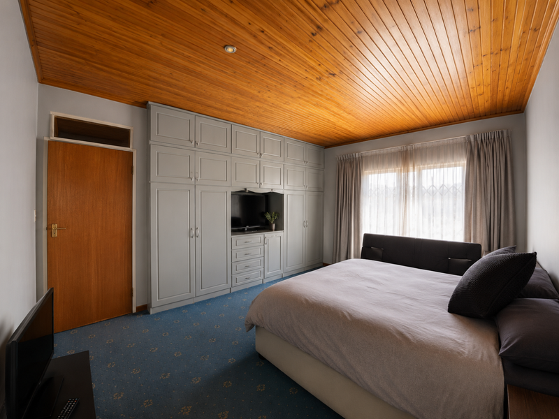 Spacious bedroom featuring extensive built-in cabinetry, a warm timber tongue and groove ceiling, and large windows with security gates.