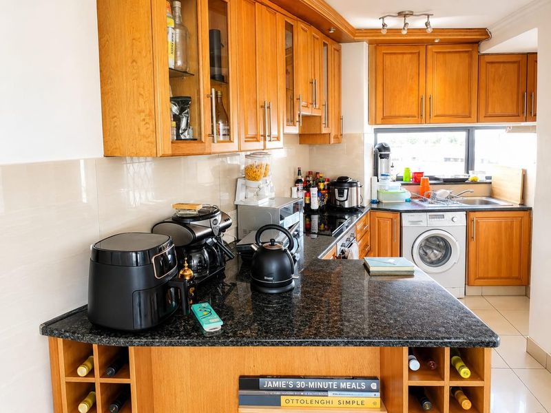 A functional kitchen featuring warm wooden cabinetry, dark granite countertops, a built-in washing machine, and a convenient integrated wine rack.