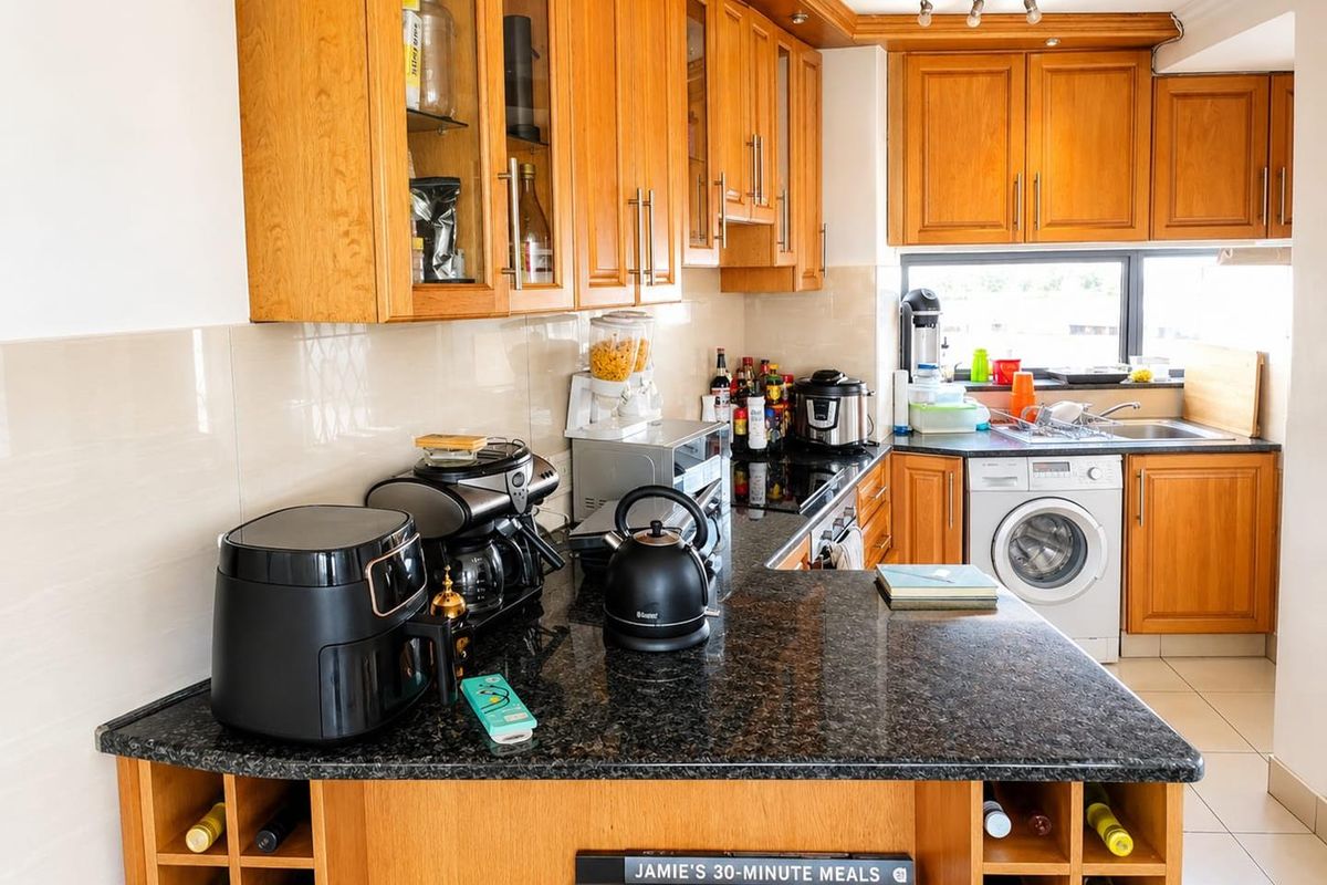 A functional kitchen featuring warm wooden cabinetry, dark granite countertops, a built-in washing machine, and a convenient integrated wine rack.