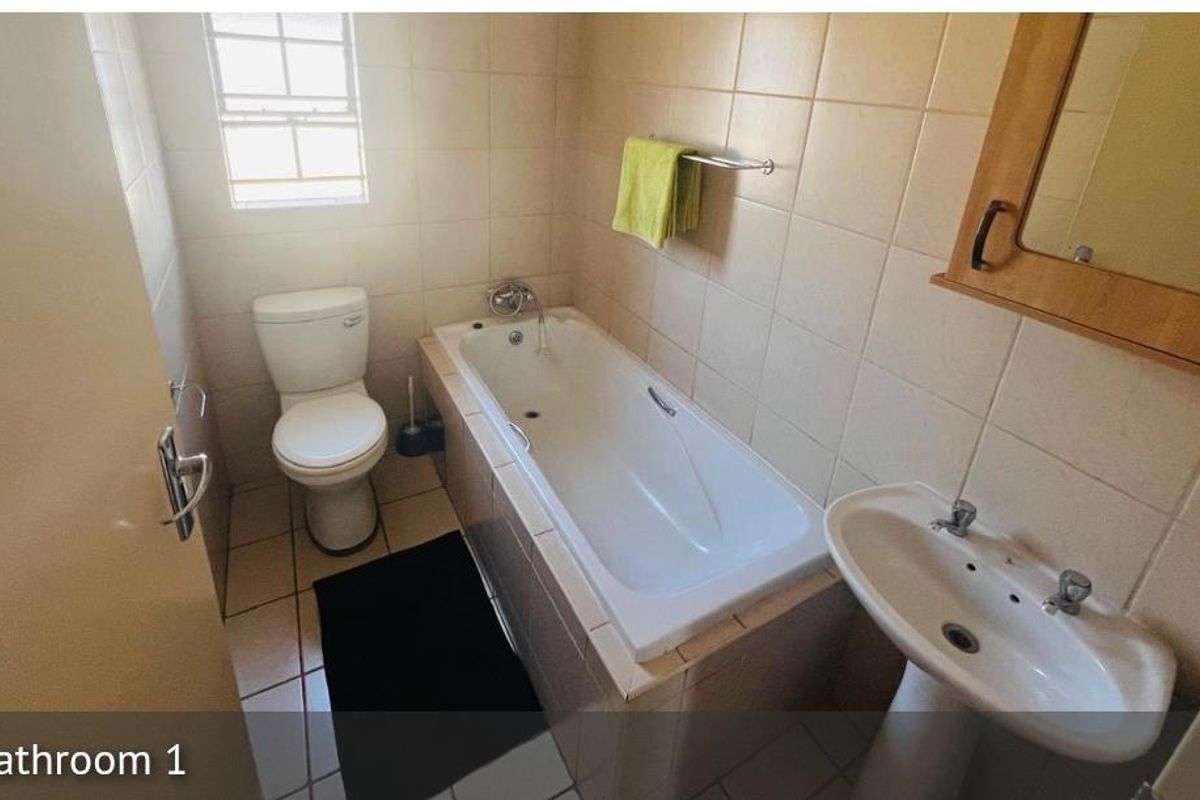 A functional bathroom featuring a built-in bathtub, pedestal basin, and toilet with neutral wall tiling.
