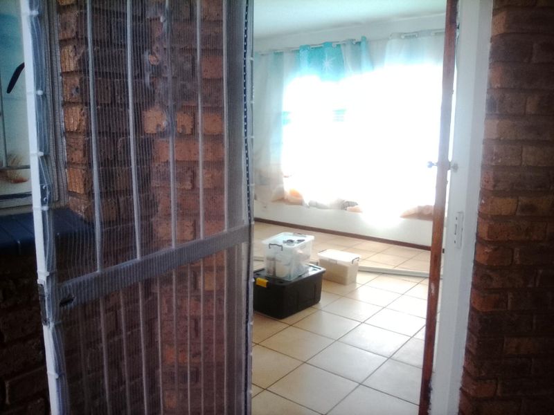An interior view of a living area featuring ceramic floor tiles and exposed brick walls, viewed through a doorway with a screen.