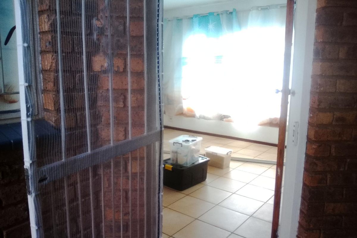 An interior view of a living area featuring ceramic floor tiles and exposed brick walls, viewed through a doorway with a screen.