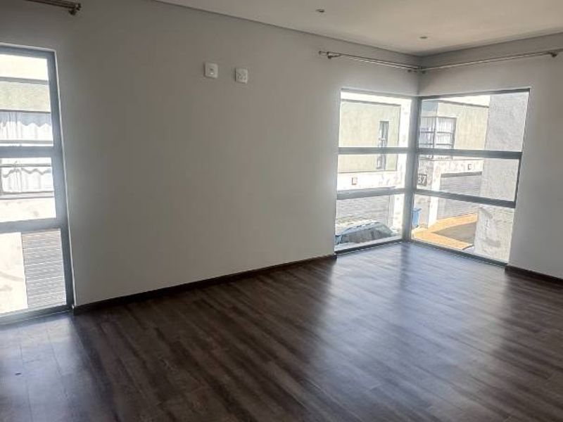 A bright and spacious living area featuring modern laminate flooring, recessed downlights, and large windows that provide ample natural light.