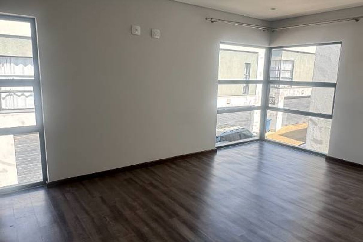 A bright and spacious living area featuring modern laminate flooring, recessed downlights, and large windows that provide ample natural light.