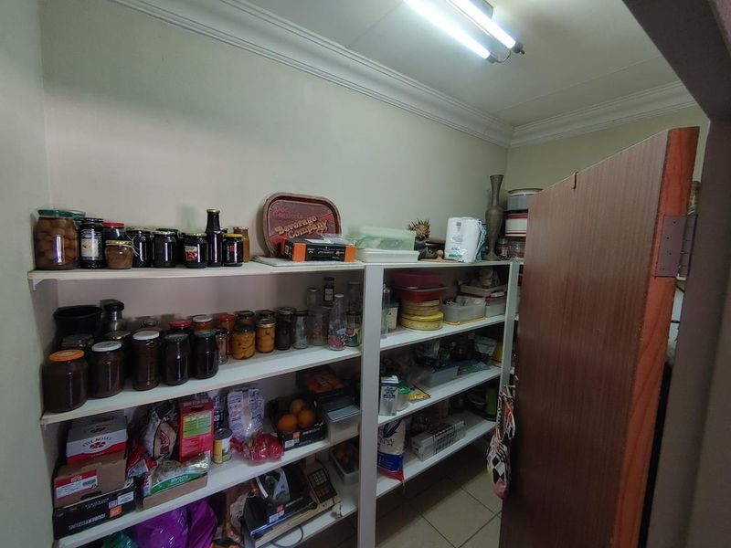 A functional walk-in pantry or scullery area featuring extensive built-in shelving for storage and tiled flooring.