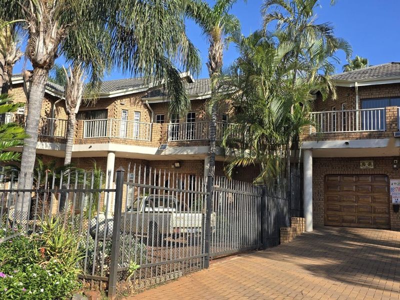 Front elevation of a double-story brick house featuring a paved driveway, double garage, and upper-level balcony with metal railings.