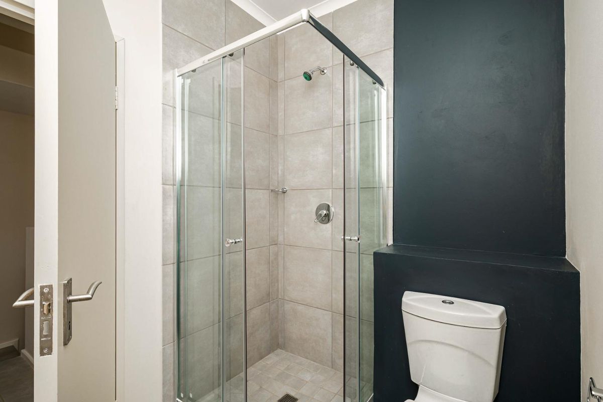 A modern bathroom featuring a glass-enclosed shower with neutral wall tiling and a contrasting dark feature wall behind the toilet.