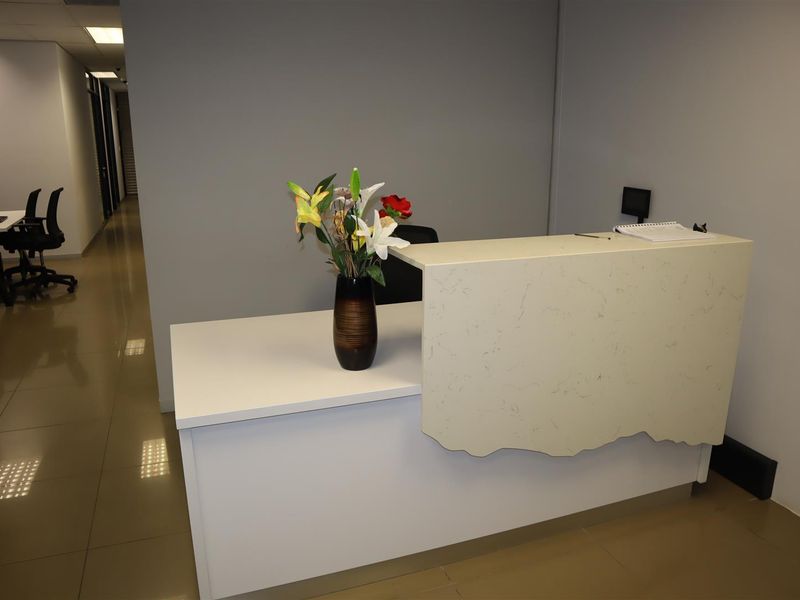 A professional office reception area featuring a modern reception desk, tiled flooring, and recessed ceiling lighting.