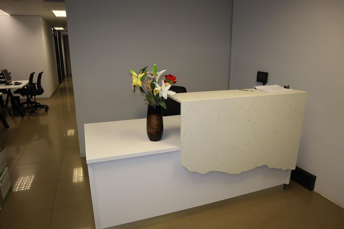 A professional office reception area featuring a modern reception desk, tiled flooring, and recessed ceiling lighting.