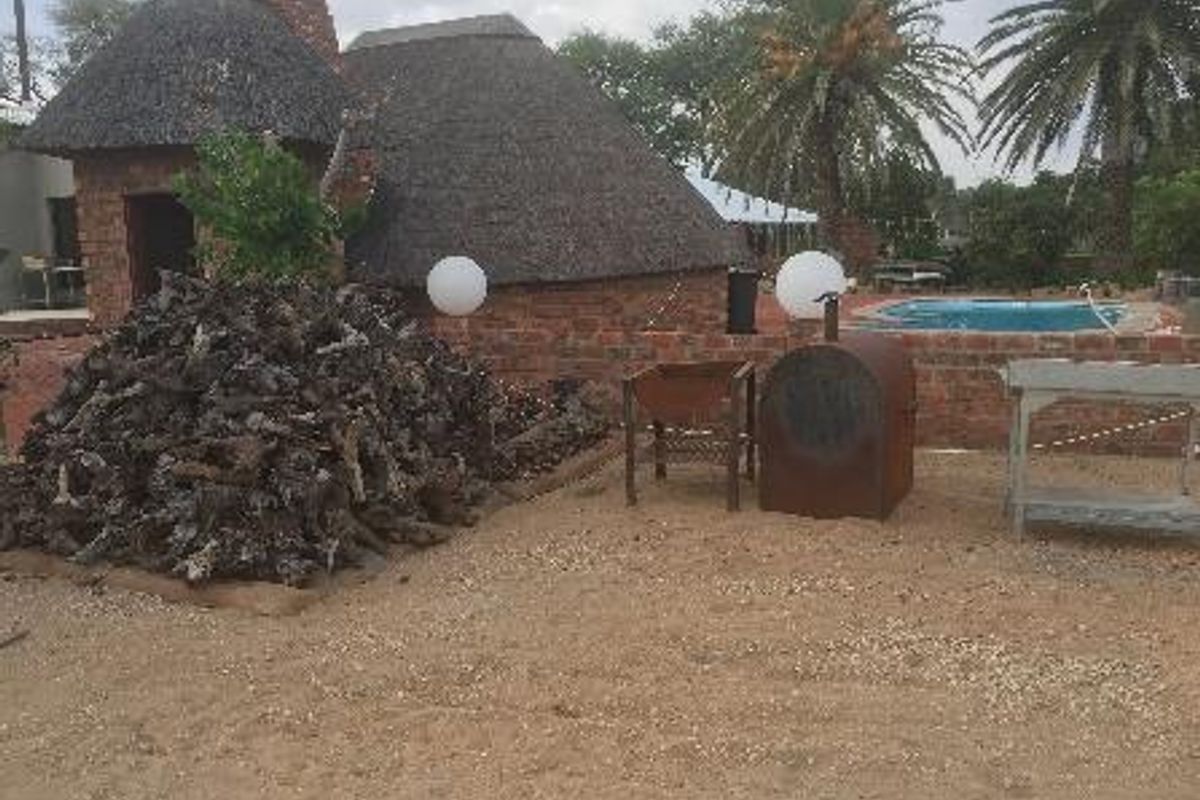 Outdoor entertainment area featuring a thatched roof structure, brick walling, and a swimming pool in the background.