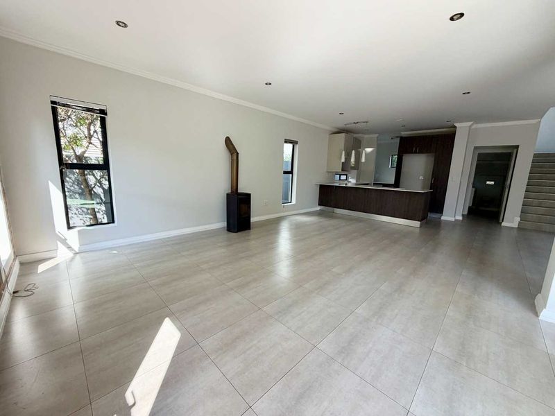 Spacious open-plan living area featuring large format floor tiles, a modern kitchen with island, and a freestanding fireplace, offering a bright and versatile layout.