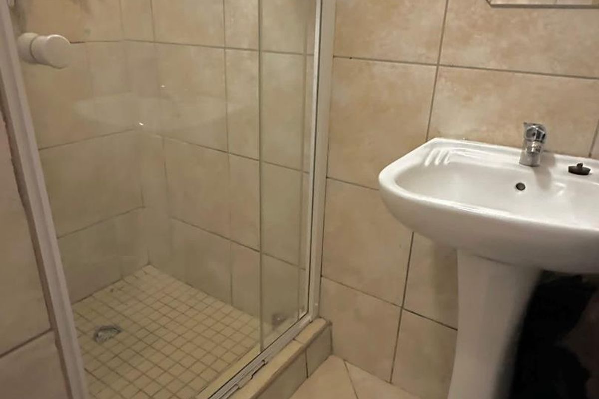 A compact bathroom featuring a pedestal sink, a glass-enclosed shower, and neutral wall and floor tiling.
