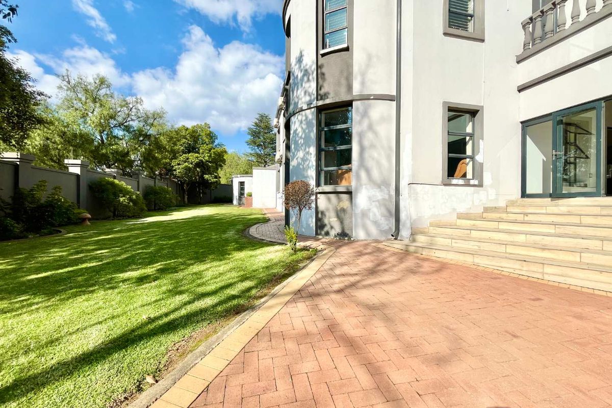 Rear view of the property featuring a paved patio area, landscaped lawn, boundary wall, and access to the main house via stone stairs.