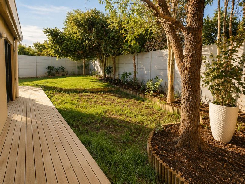 A private rear garden featuring a timber deck, established trees, and a secure precast concrete boundary wall.