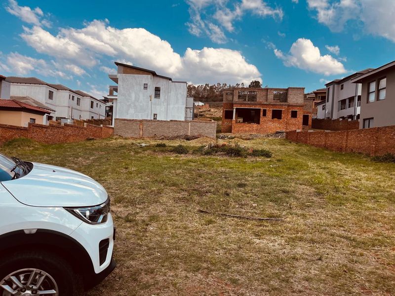 A vacant residential plot enclosed by brick boundary walls, situated in a developing neighborhood with surrounding residential construction.