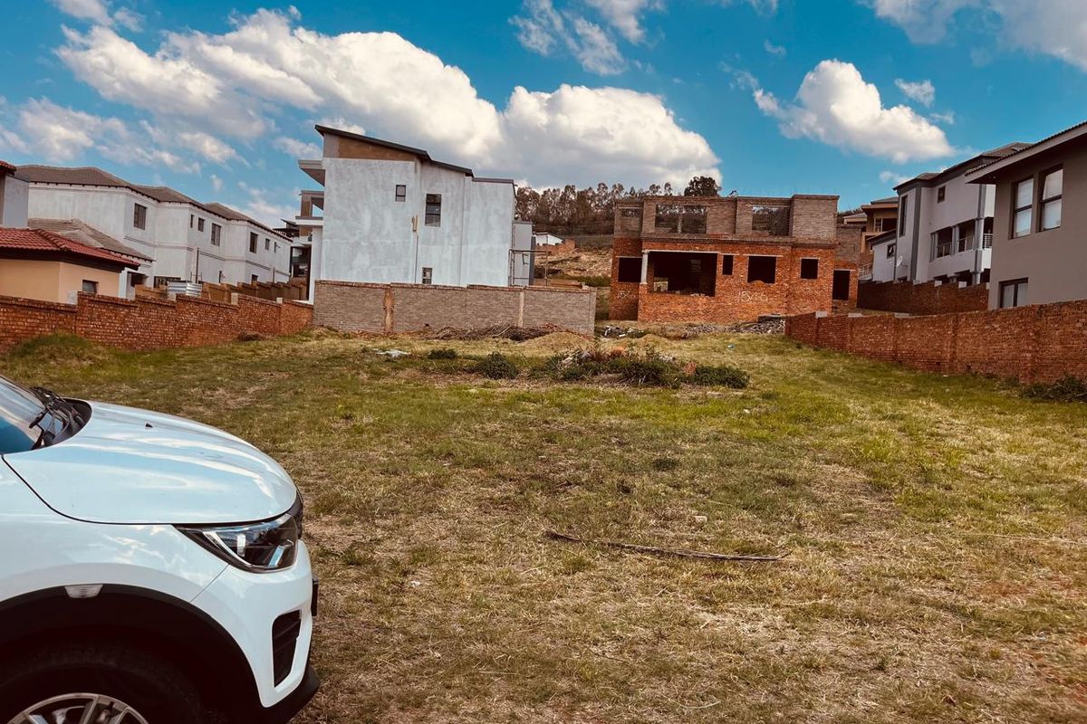 A vacant residential plot enclosed by brick boundary walls, situated in a developing neighborhood with surrounding residential construction.