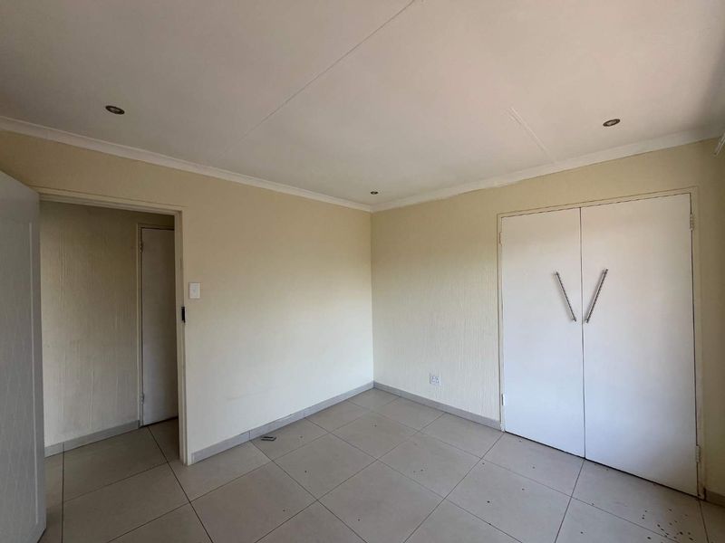 An empty bedroom featuring neutral tiled flooring, built-in cupboards, and recessed ceiling lighting, offering a clean canvas for personalization.