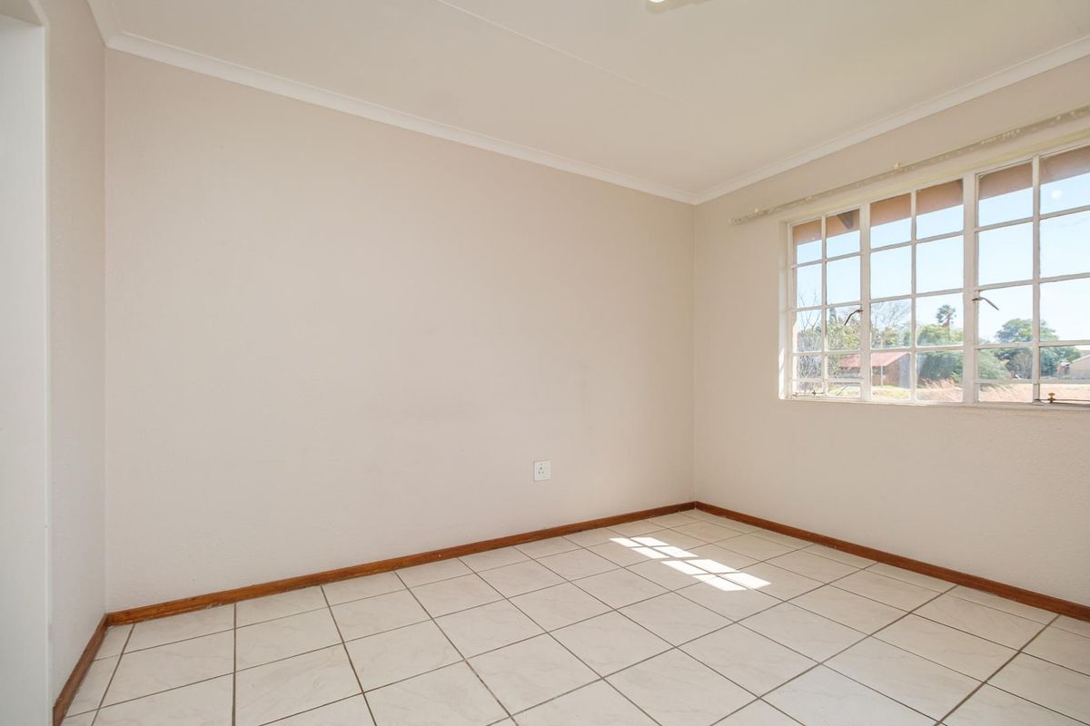 A bright, empty bedroom featuring neutral walls, tiled flooring, and a large grid-pattern window allowing for natural light.