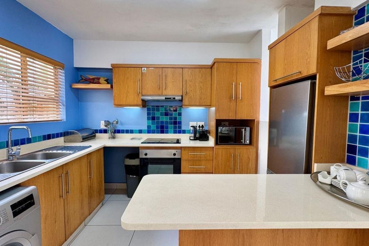 A functional kitchen featuring wooden cabinetry, stone countertops, a tiled splashback, and integrated appliances including an oven and hob.