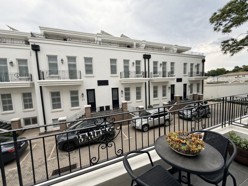 A view from a private balcony overlooking the paved driveway and the exterior facade of a modern multi-level townhouse complex.