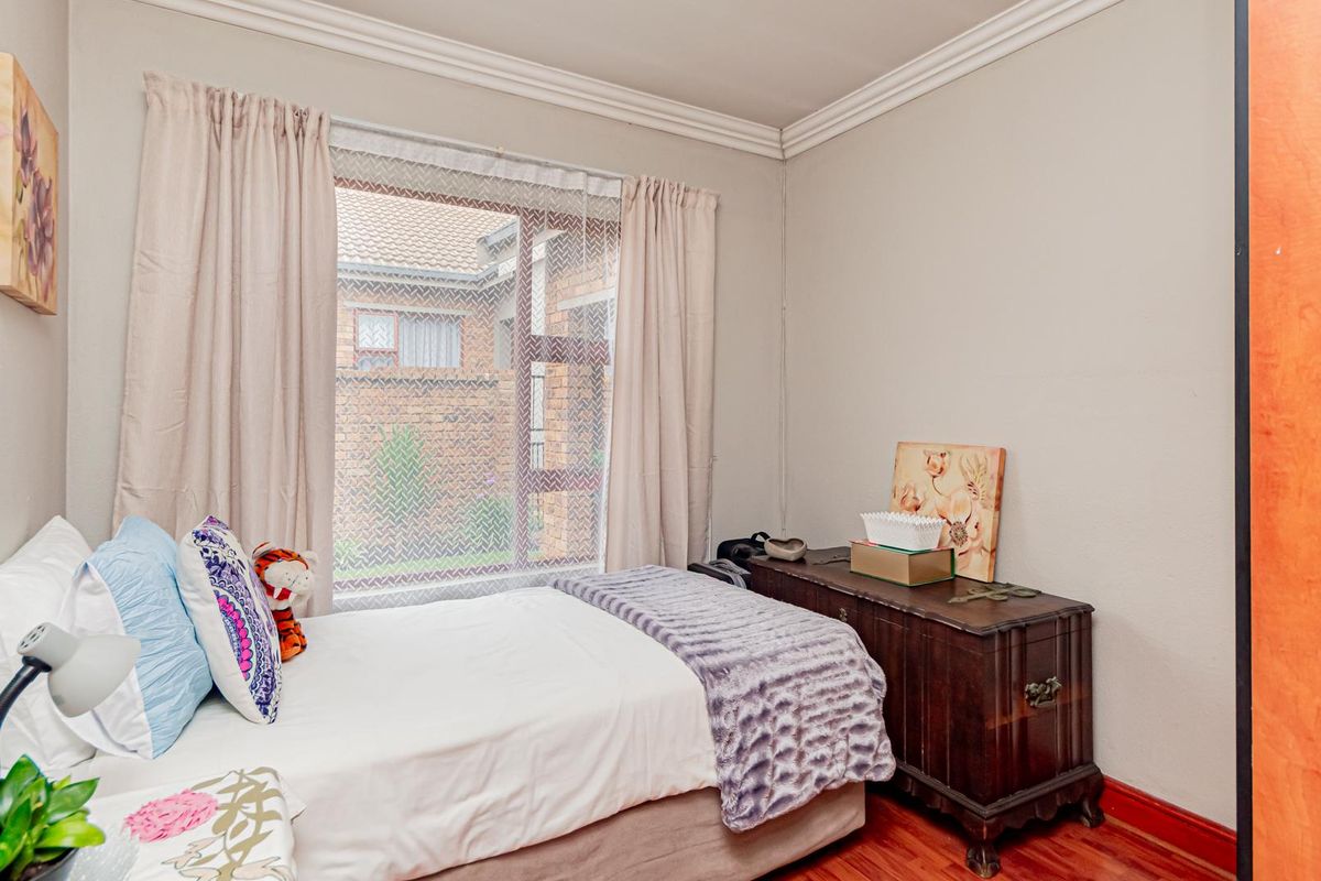 A cozy bedroom featuring warm-toned wood flooring, crown molding, and a window providing natural light and a view of the exterior brickwork.