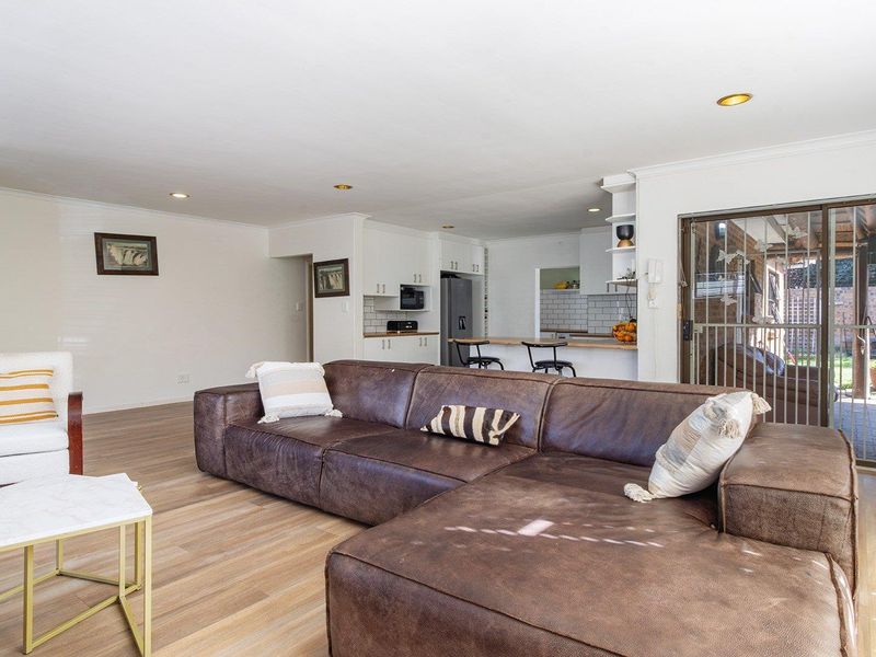 Spacious open-plan living area featuring laminate flooring, recessed lighting, and a functional kitchen with a breakfast bar and direct access to the patio.