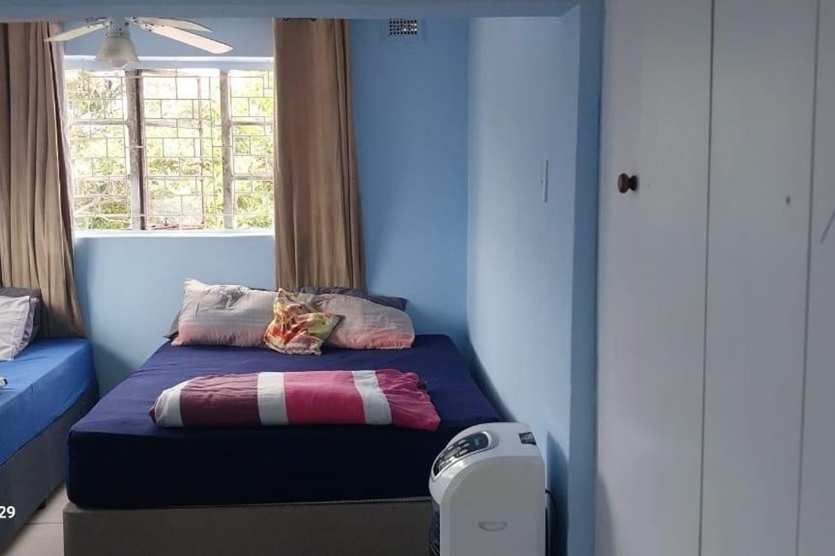 A bedroom featuring built-in cupboards, a ceiling fan, and security bars on the window.