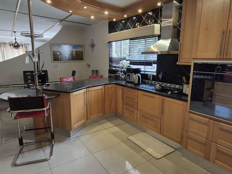 Open plan kitchen featuring wooden cabinetry, granite countertops, built-in oven, and stainless steel extractor fan, seamlessly flowing into the adjacent dining area.