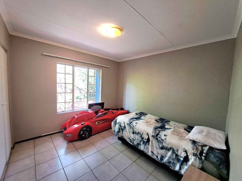 A standard bedroom featuring tiled flooring, a built-in cupboard, and a window providing natural light.