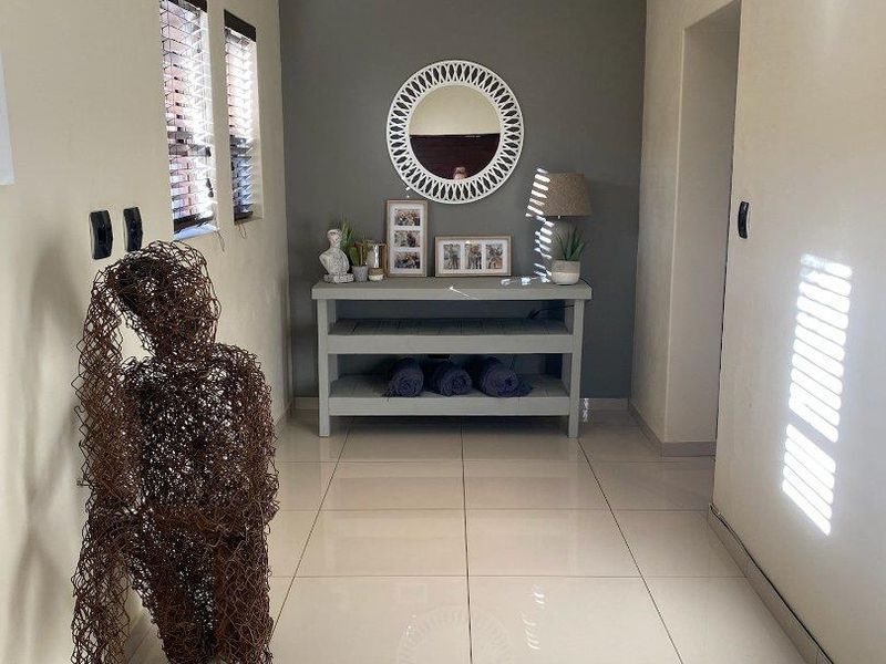 A bright and well-maintained hallway featuring polished tiled flooring, recessed downlighting, and a neutral color palette with a contrasting feature wall.