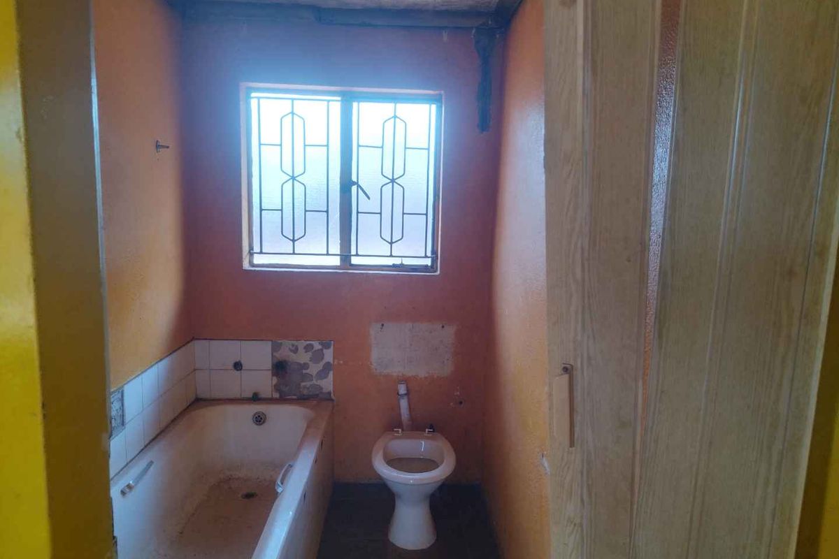 A dated bathroom featuring a bathtub, toilet, and security-barred window, requiring significant renovation and cosmetic updates to improve functionality and aesthetic appeal.