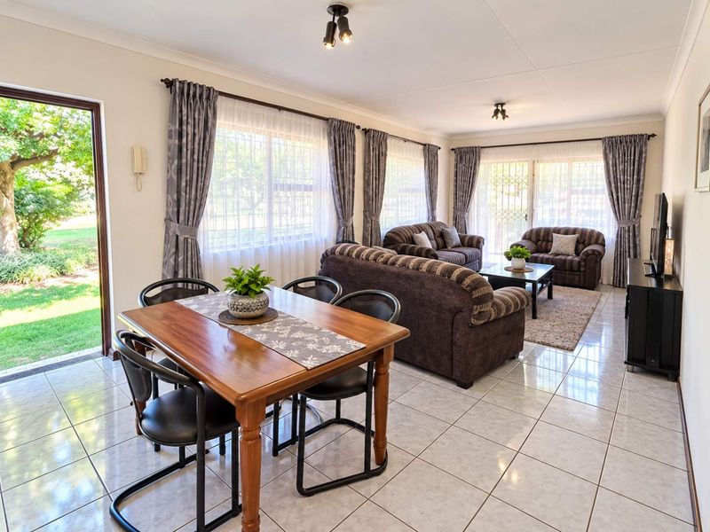 Spacious open-plan living and dining area featuring neutral tiled flooring, large windows with natural light, and direct access to the garden through sliding doors.