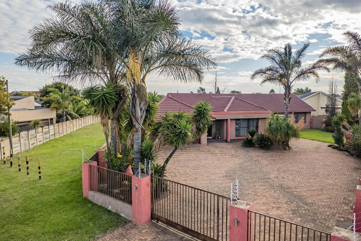 Aerial view of a residential property featuring a paved driveway, tiled roof, and established garden with perimeter fencing and security features.