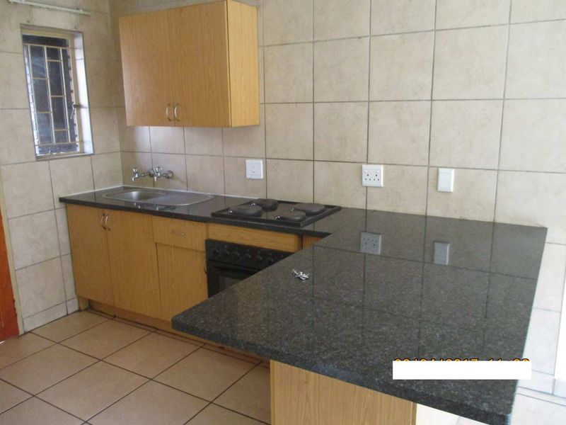 A functional kitchen featuring granite countertops, built-in oven and hob, wall-mounted cabinetry, and tiled finishes throughout.