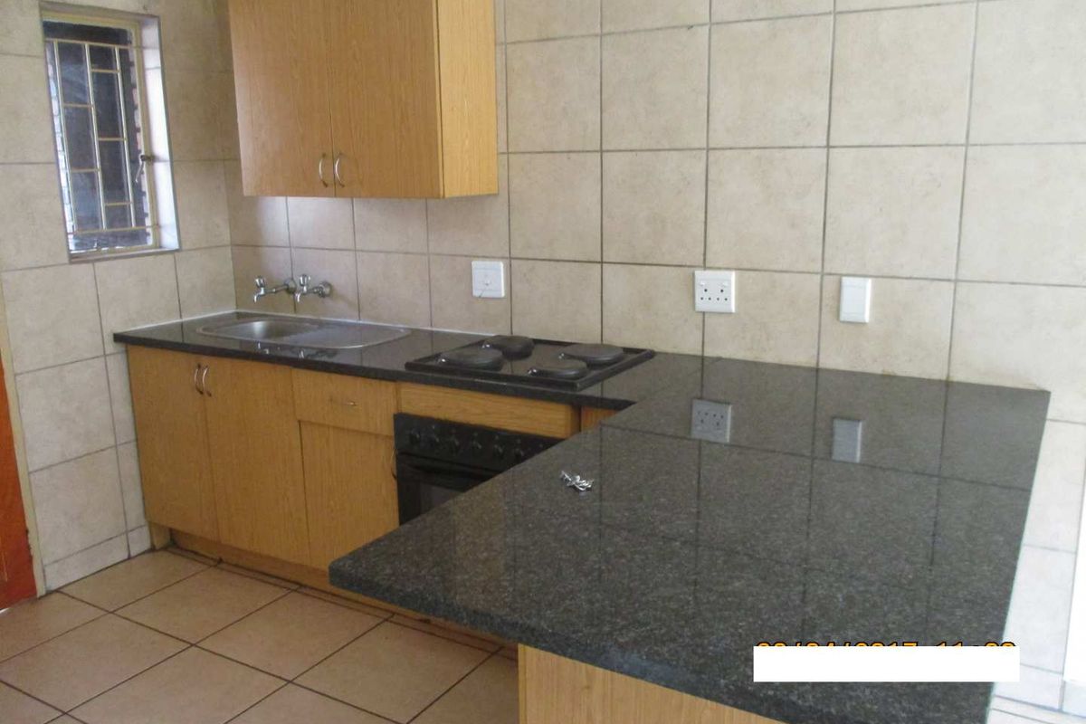 A functional kitchen featuring granite countertops, built-in oven and hob, wall-mounted cabinetry, and tiled finishes throughout.