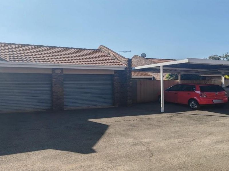 Front exterior view of the townhouse featuring a double garage and an attached carport with paved driveway space.
