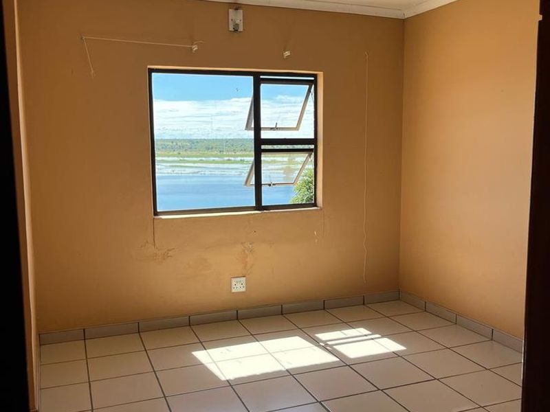 An empty bedroom featuring tiled flooring, neutral wall paint, and an aluminium window frame with a view.