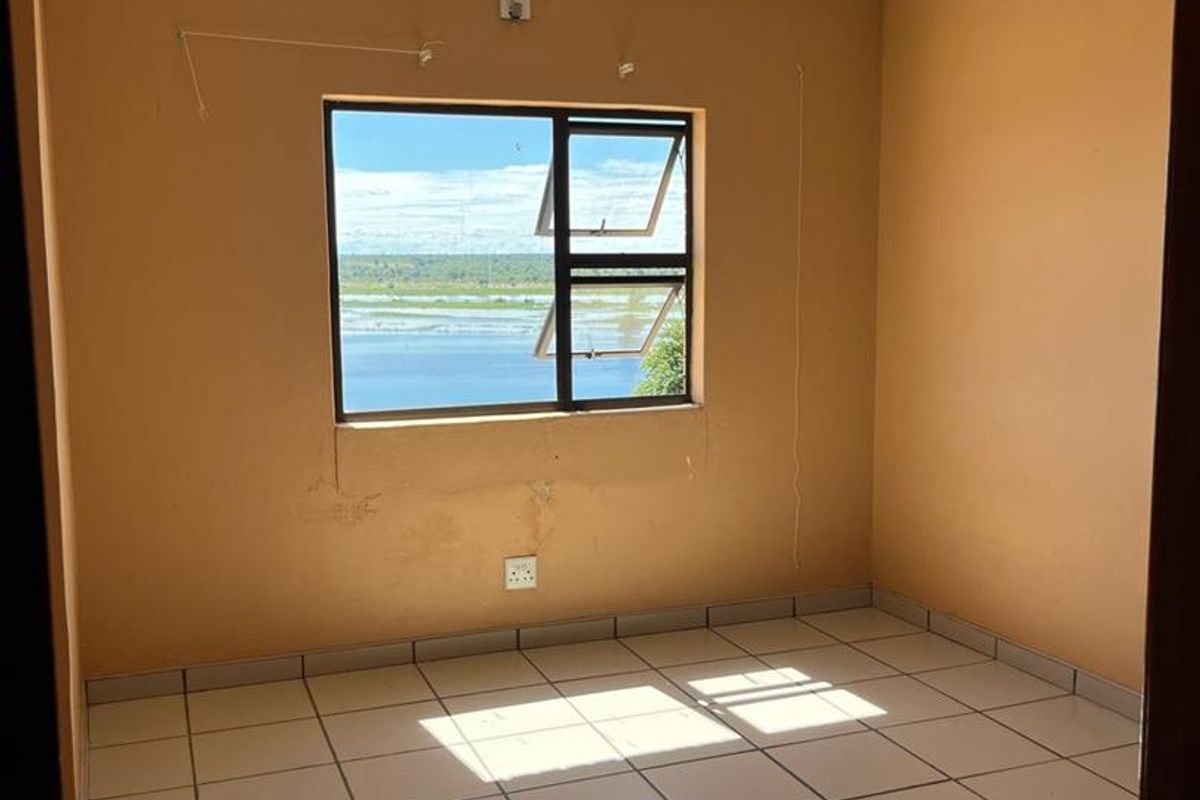 An empty bedroom featuring tiled flooring, neutral wall paint, and an aluminium window frame with a view.