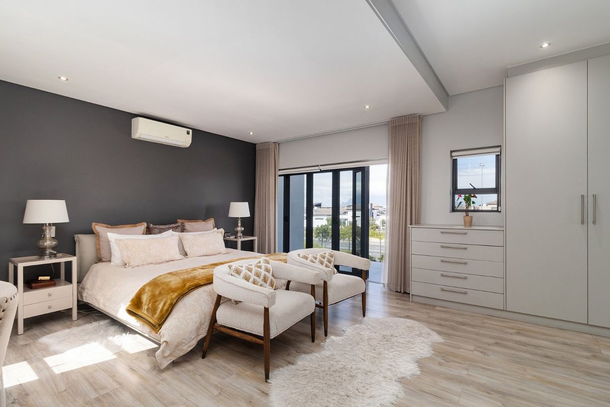 Spacious modern bedroom featuring laminate flooring, built-in cupboards, recessed lighting, a split-system air conditioner, and sliding doors leading to an outdoor area.