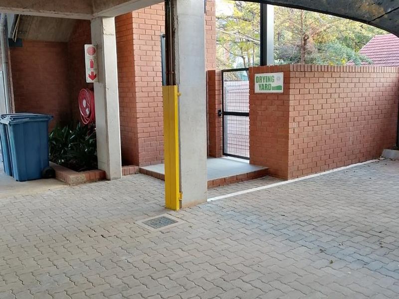 A paved utility area featuring concrete structural pillars, a brick boundary wall, and a gated entrance leading to a drying yard.