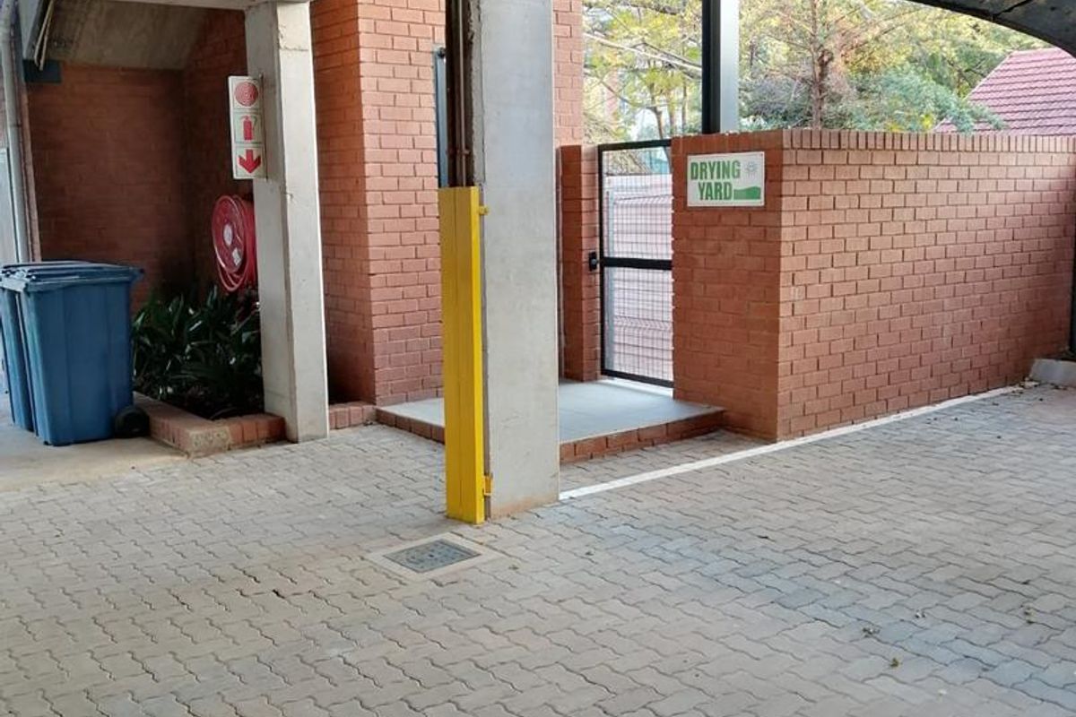 A paved utility area featuring concrete structural pillars, a brick boundary wall, and a gated entrance leading to a drying yard.